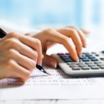 Detalhe de mão utilizando caneta e calculadora, simbolizando a revisão fiscal para evitar erros contábeis e prejuízos financeiros em empresas, serviço da Liz Consultoria em Campinas-SP.