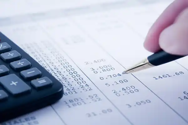 Detalhe de profissional contábil realizando fechamento de balanço e análise de demonstrações financeiras com calculadora em escritório em Campinas-SP.