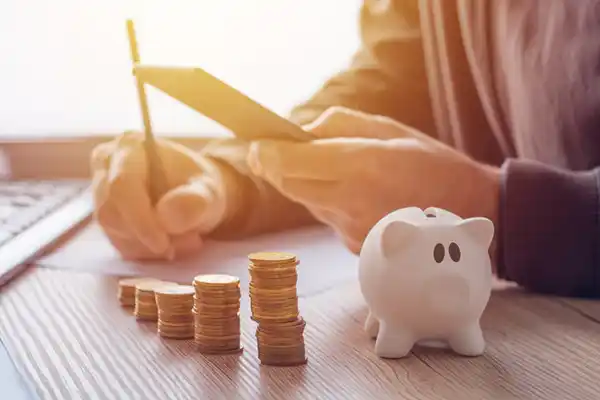 Pessoa consultando aplicativo financeiro no celular com cofrinho de porco e moedas na mesa, simbolizando o planejamento financeiro e redução de impostos da Liz Consultoria em Campinas-SP.